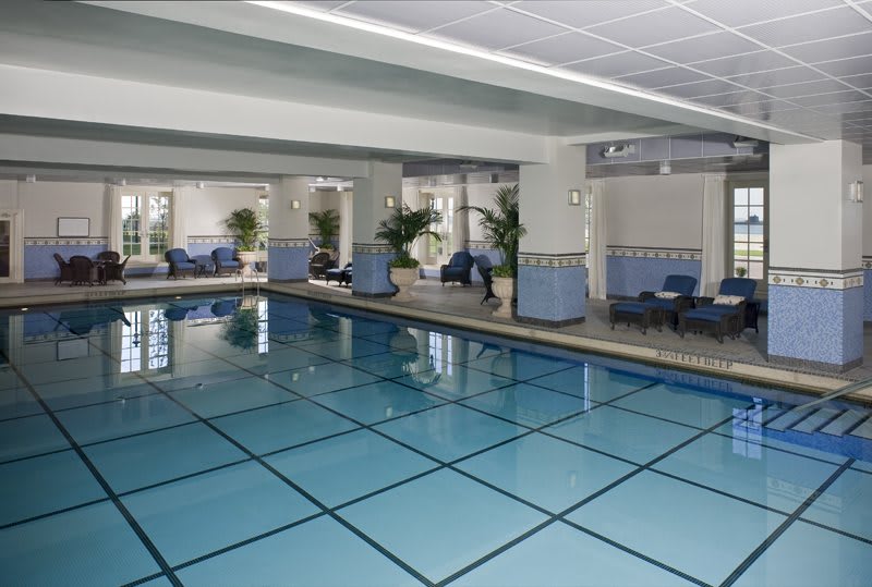 A serene indoor swimming pool area with lounge chairs and potted plants.