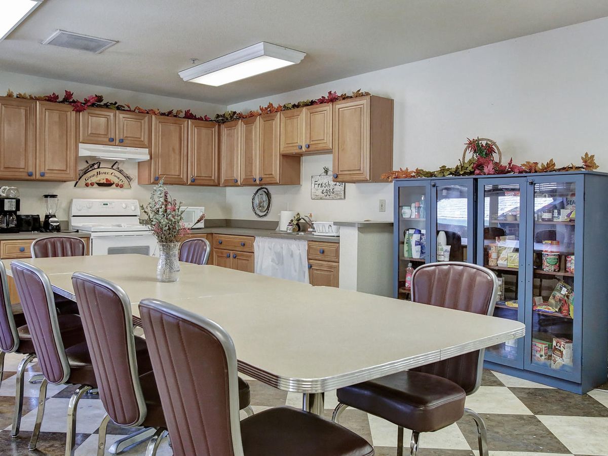 A cozy kitchen interior featuring a dining area with a large table and several chairs, surrounded by wooden cabinets and kitchen appliances.