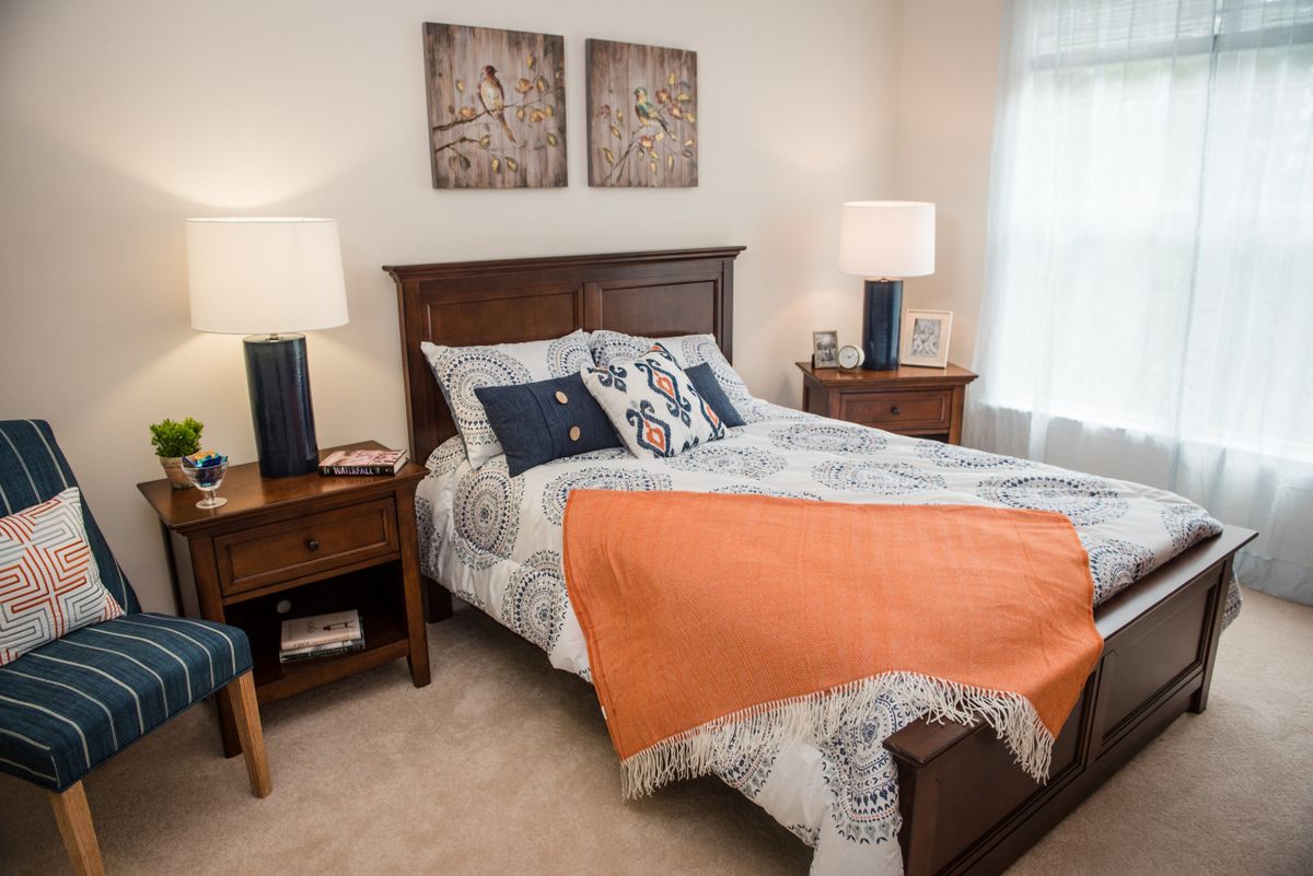 A cozy bedroom with a neatly made bed, featuring patterned bedding and an orange blanket, flanked by wooden nightstands with lamps.