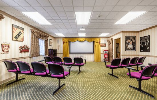 A small conference room with a projector screen and rows of chairs.
