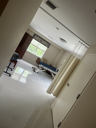 A view of a hospital room from the corridor, showcasing a patient bed and natural light coming through the window.
