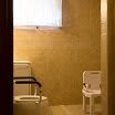 An accessible bathroom with a toilet, handrails, and a chair.