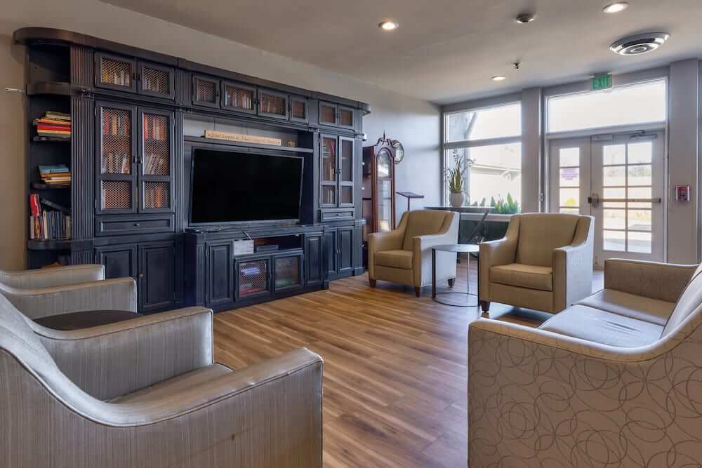 A cozy living room with a large TV, bookshelves, and comfortable armchairs.