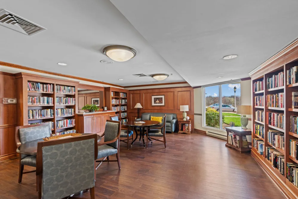 A cozy library reading area with bookshelves, comfortable seating, and large windows allowing natural light.
