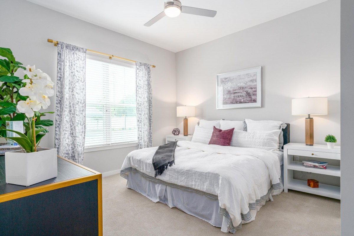 A bright and cozy bedroom with white bedding, nightstands, lamps, and a ceiling fan.