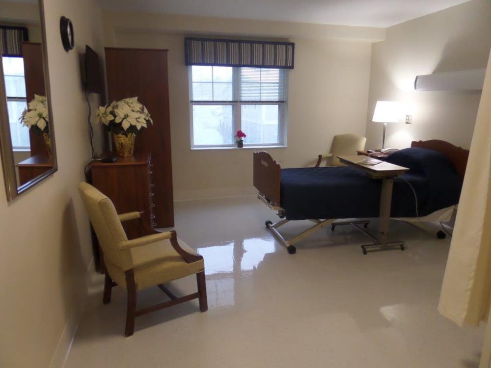A clean and well-lit hospital room with a bed, chair, and decorations.