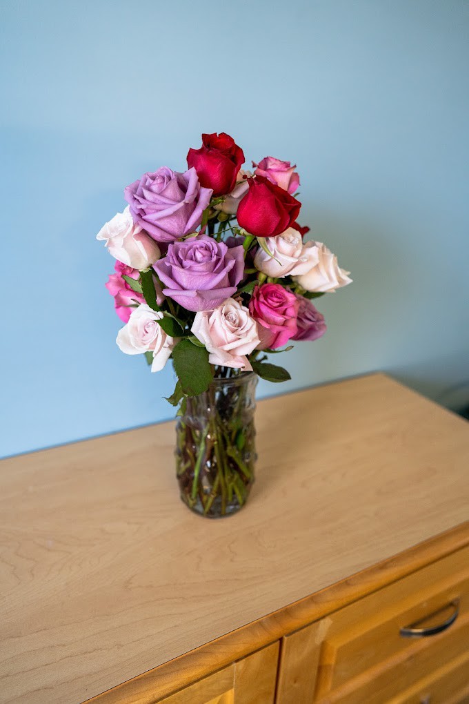 A colorful bouquet of roses in a clear glass vase on a wooden surface.