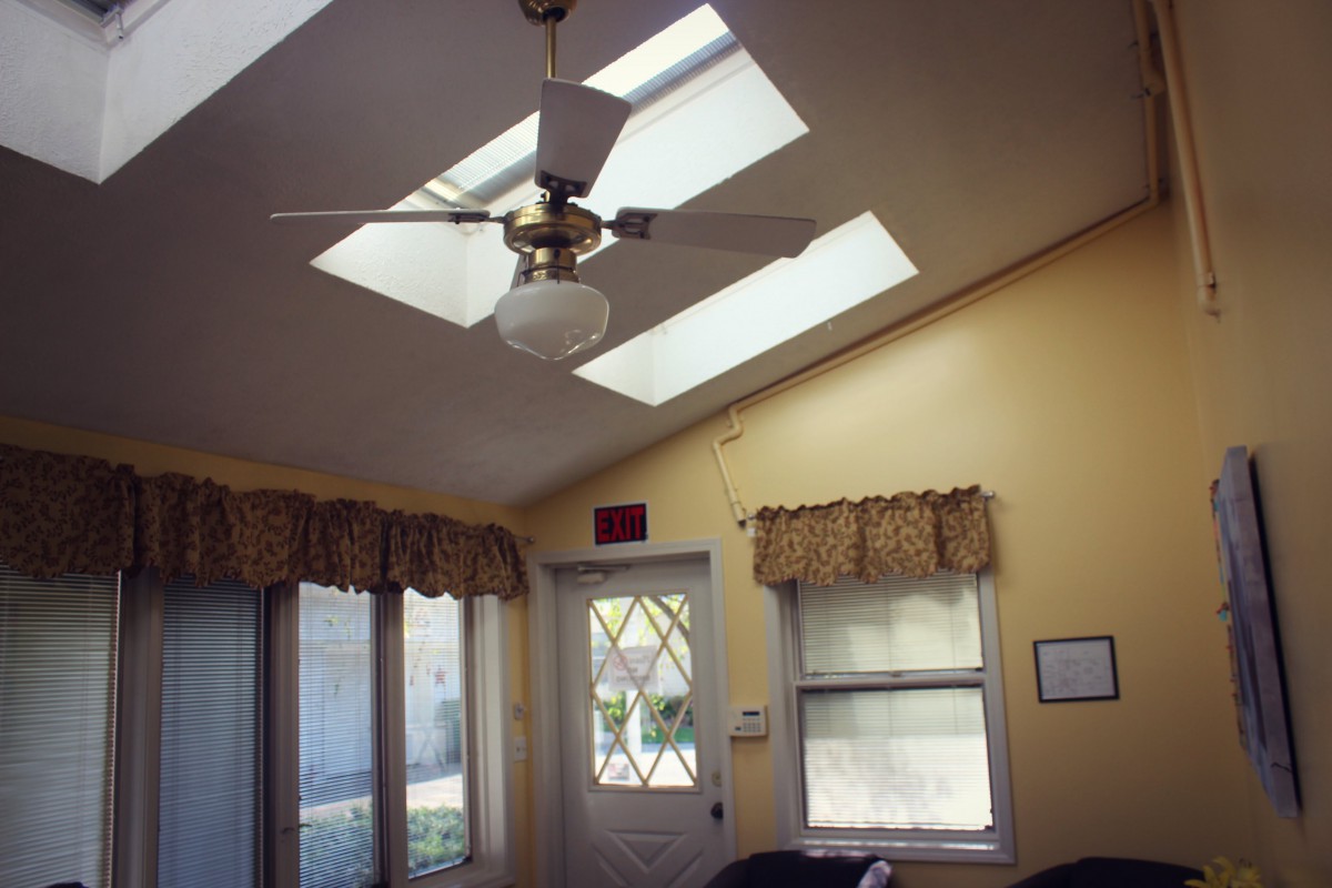 A bright room with skylights, a ceiling fan, and windows adorned with curtains.