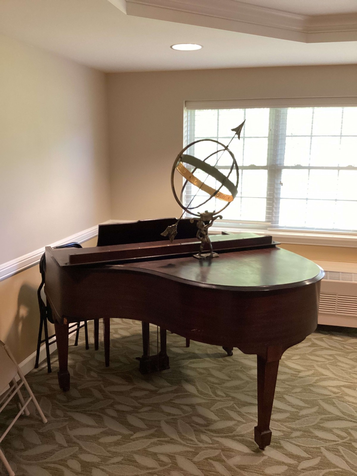 A grand piano in a well-lit room with a decorative sphere on top.