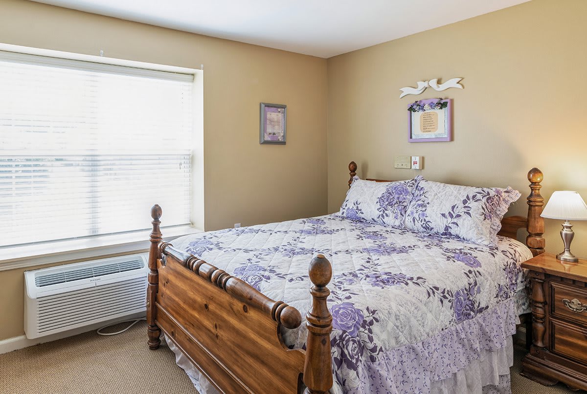 A cozy bedroom featuring a wooden bed frame with floral bedding and natural light from the window.