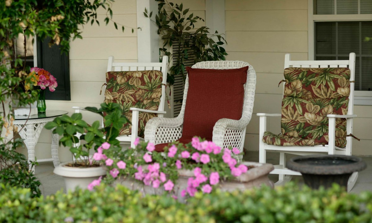 A cozy porch with wicker rocking chairs surrounded by lush greenery and vibrant pink flowers.