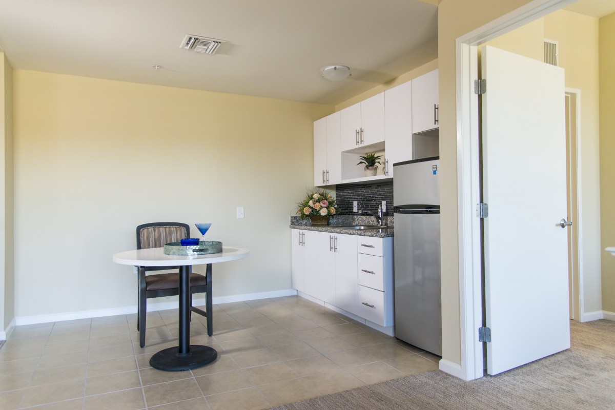 A small kitchen area with white cabinets, a stainless steel fridge, and a dining table with chairs.