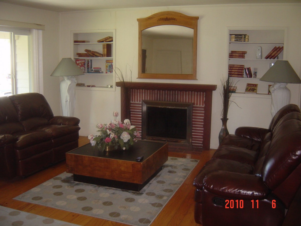A cozy living room with a fireplace, leather sofas, and a central coffee table, surrounded by built-in shelves and a mirror above the mantel.