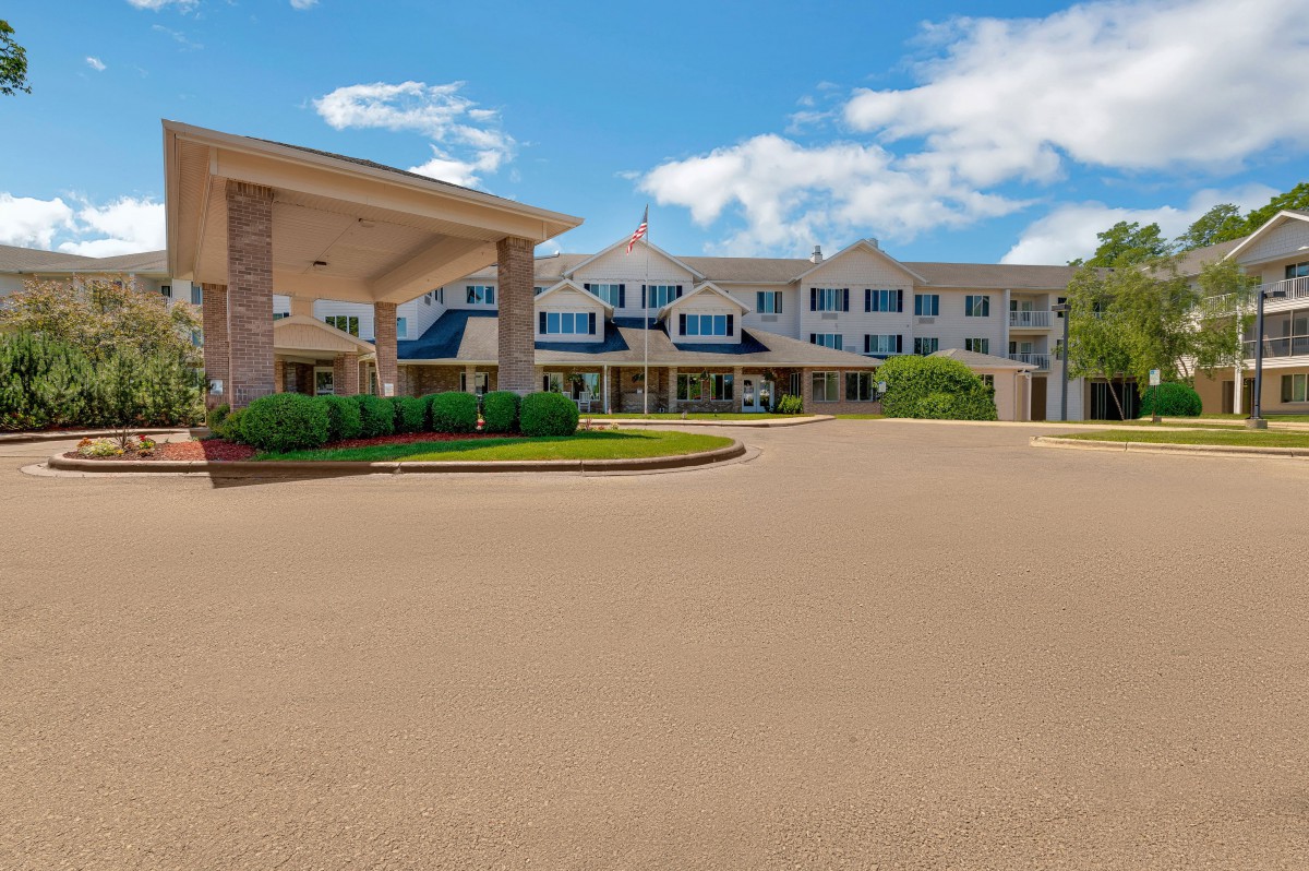A large hotel building with a spacious driveway under a bright blue sky.