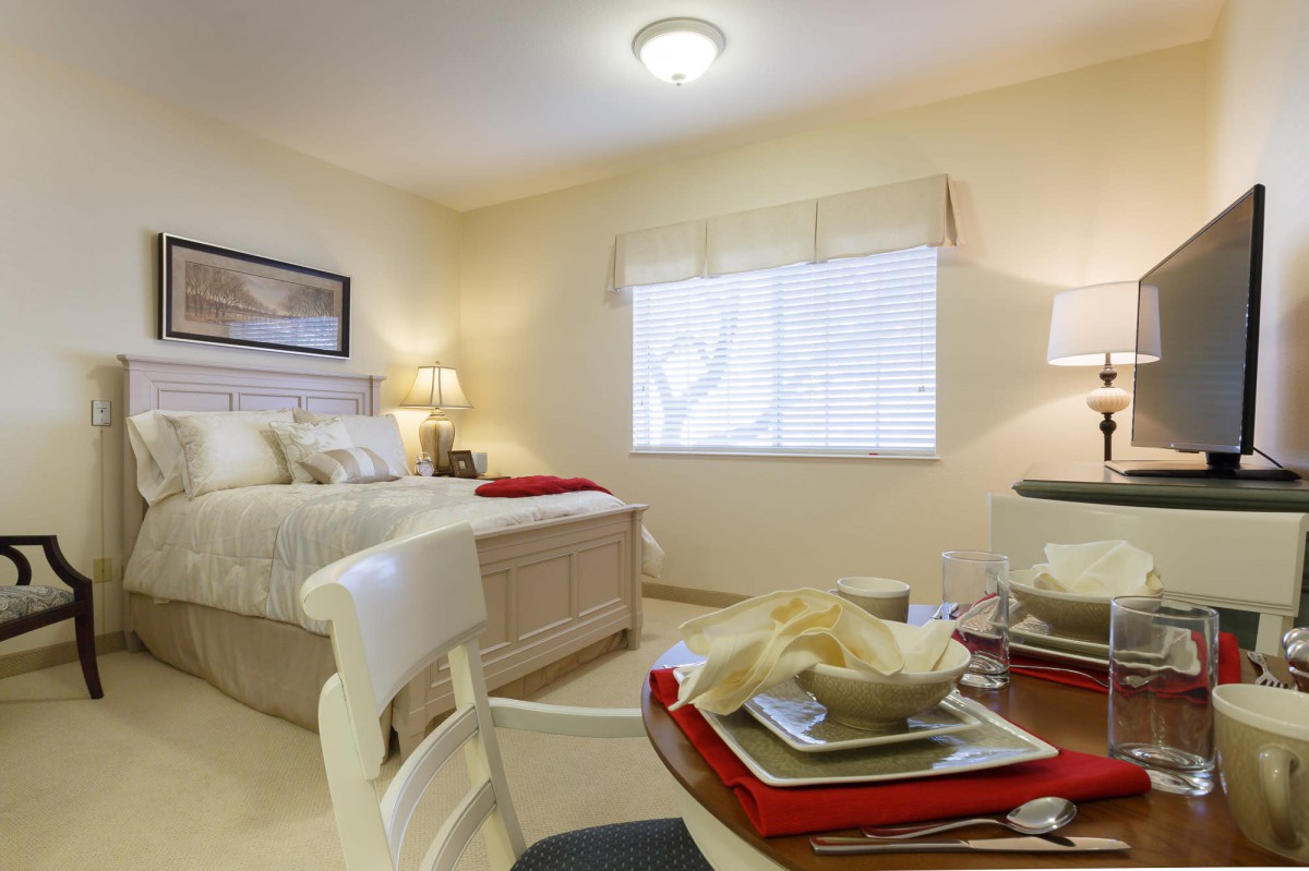 A cozy bedroom with a neatly made bed and a dining table set for two.