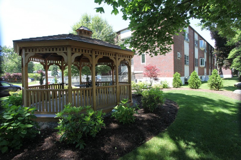 A beautiful garden scene with a wooden gazebo surrounded by lush greenery and well-manicured landscaping.
