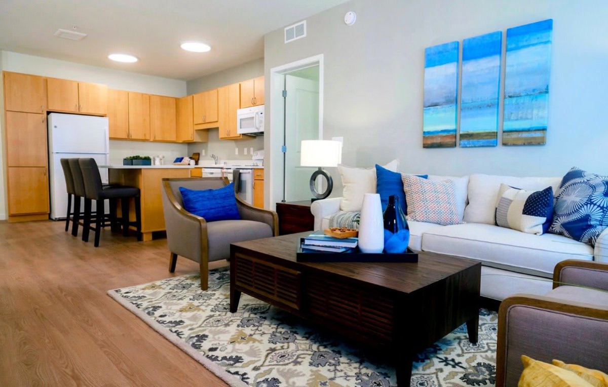 A modern living room with a view into the kitchen, featuring comfortable seating and stylish decor.