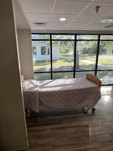 A hospital patient room featuring a bed and large windows allowing natural light to enter.