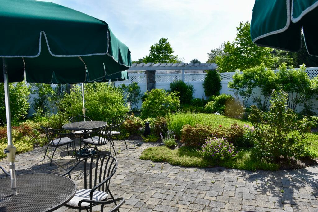 An inviting garden patio with tables, chairs, and umbrellas surrounded by lush greenery.