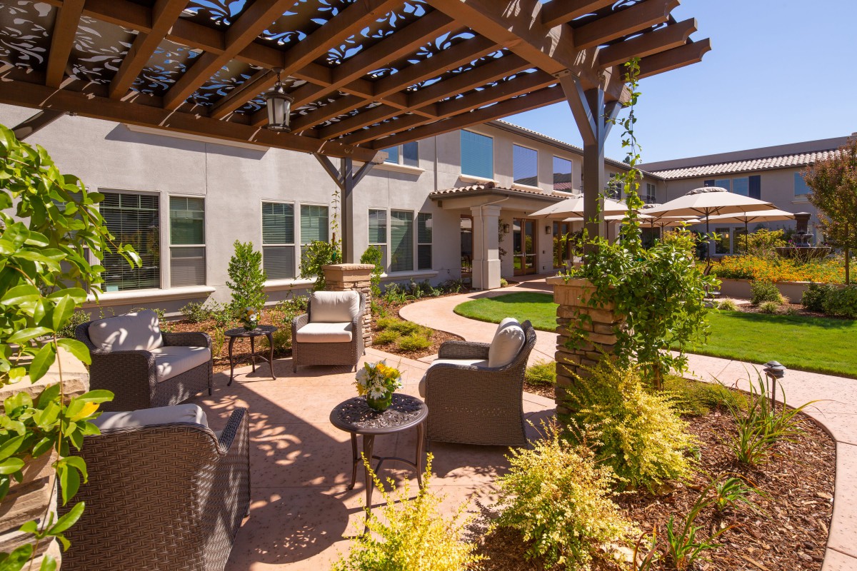 A beautifully landscaped outdoor patio area featuring a pergola, comfortable seating, and lush greenery.