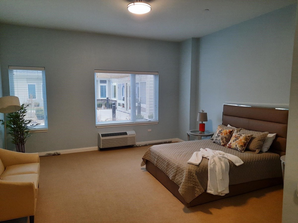 A simple and modern bedroom with a neatly made bed, a bedside table, and large windows.