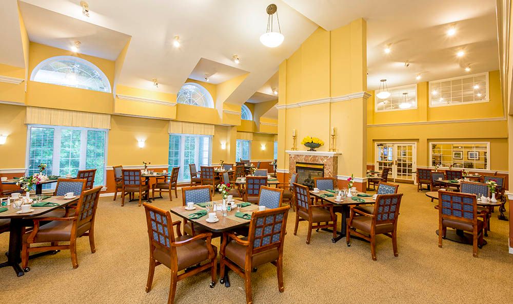 A spacious, elegantly decorated dining room with tables and chairs arranged neatly, featuring a warm color scheme and a central fireplace.