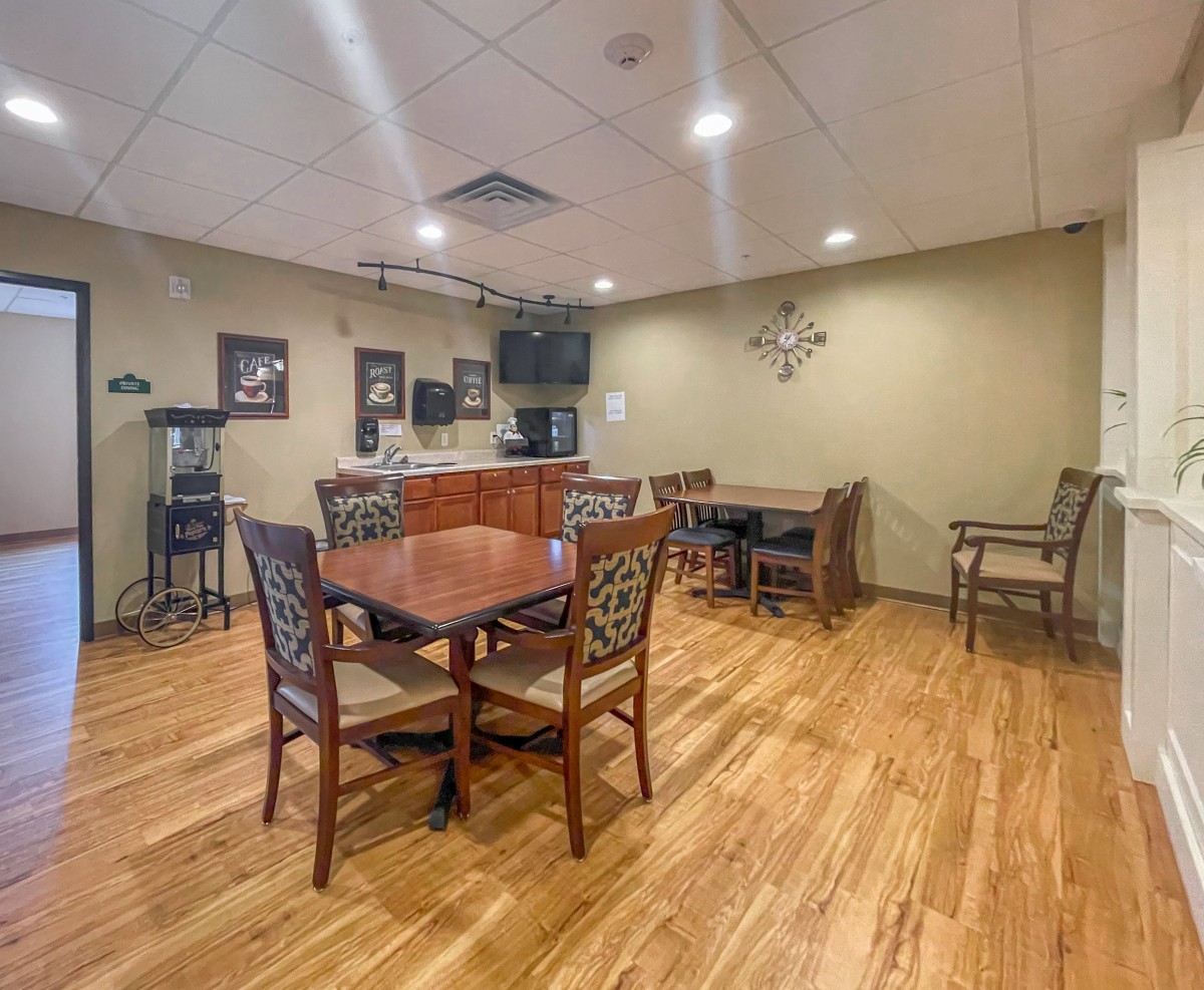 A cozy dining area with wooden flooring and furniture, featuring a table, chairs, and a television on the wall.