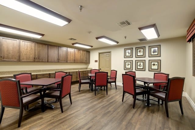 A dining room with multiple tables and chairs, wood flooring, and framed pictures on the wall.