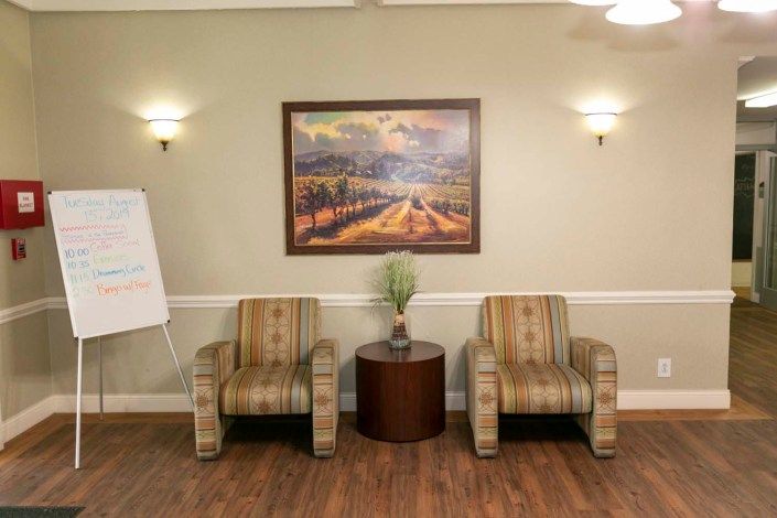 A cozy waiting area with two striped chairs, a central table with a plant, and a landscape painting on the wall.