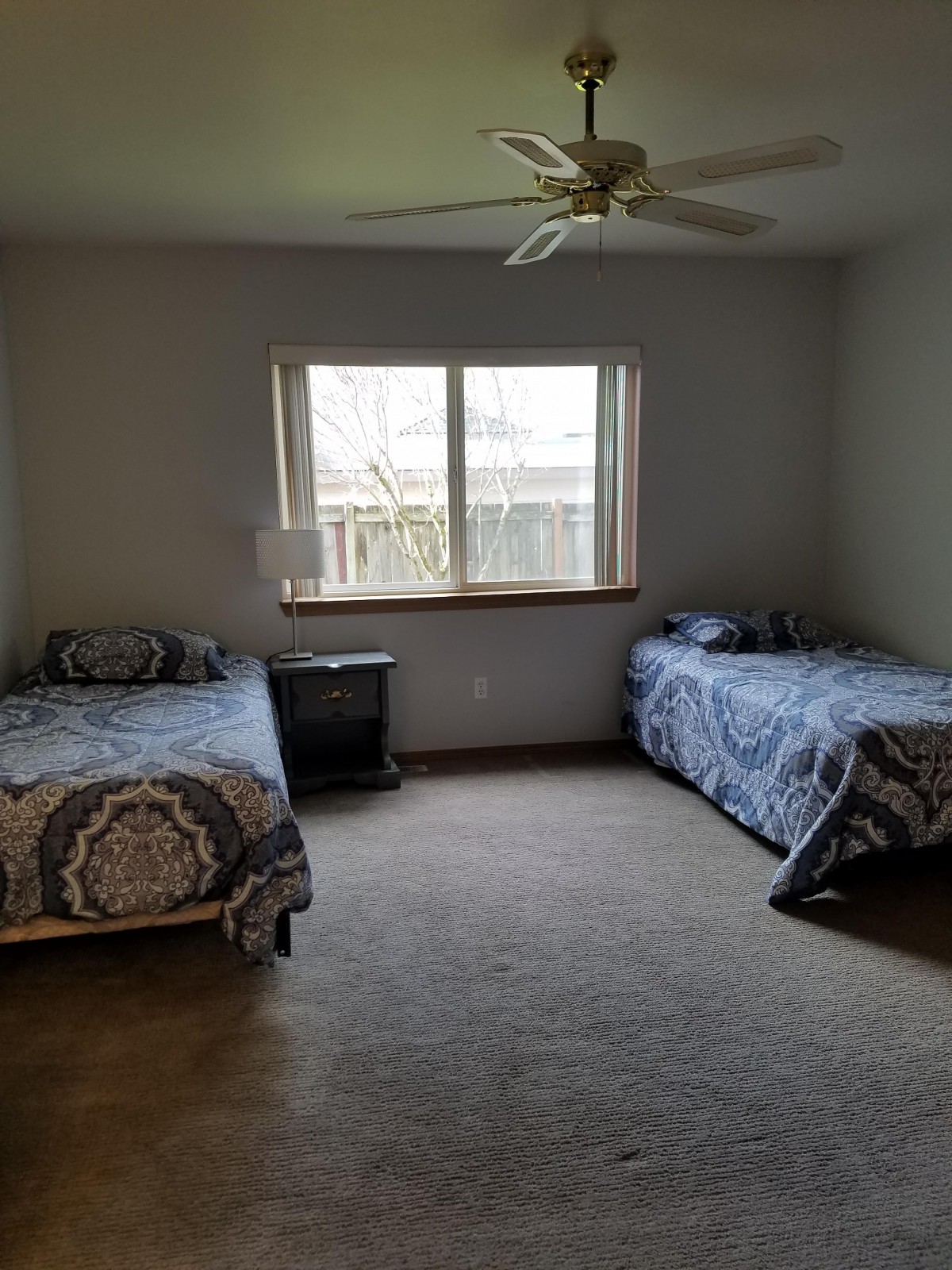 A minimalist bedroom with two twin beds, a window, and a ceiling fan.