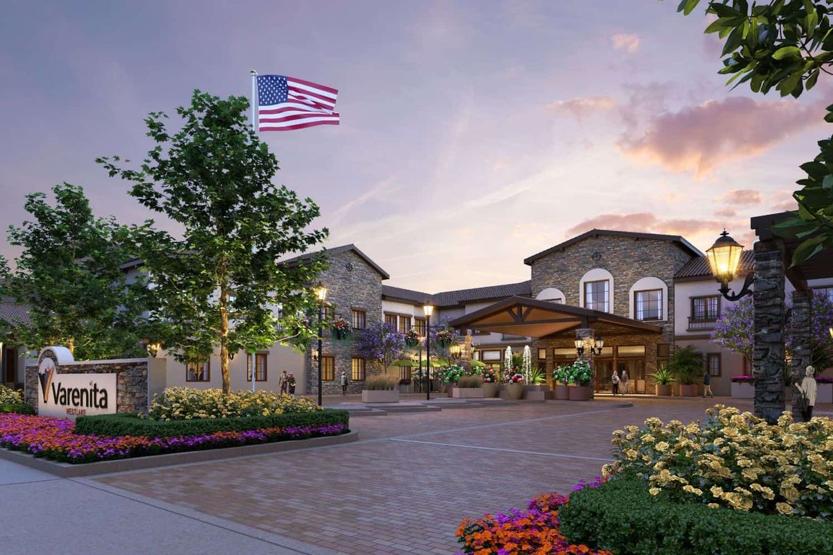 A beautifully landscaped entrance to a building at sunset, featuring an American flag and vibrant garden.