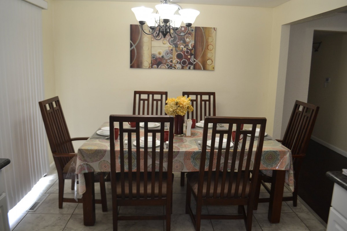 A neatly arranged dining room with a table, chairs, and a chandelier, accented by artwork and a floral centerpiece.