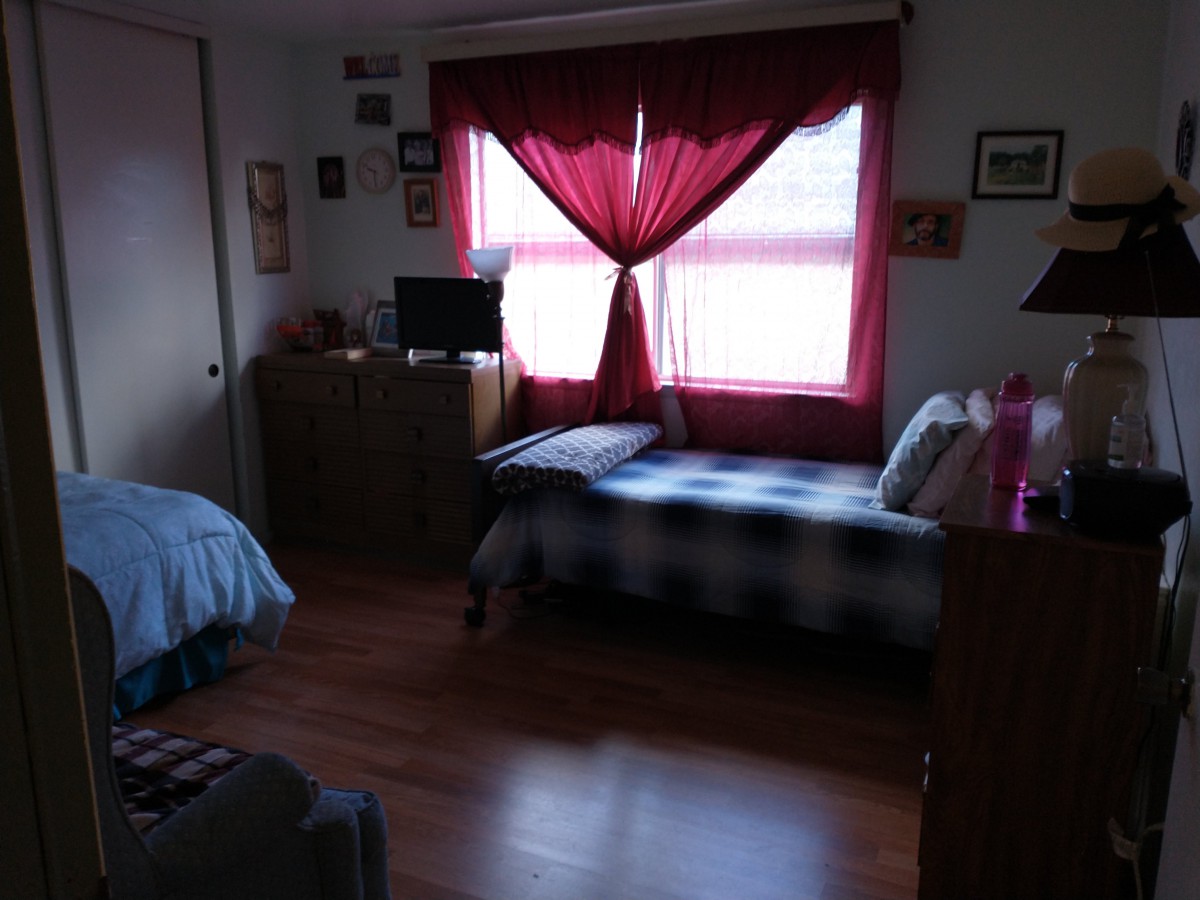 A cozy bedroom with a bed near the window, red curtains, and various furniture pieces.