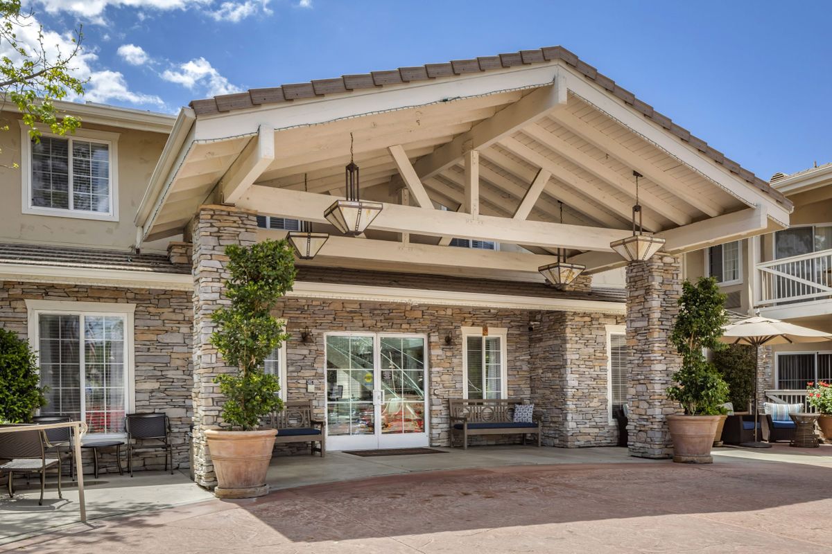 A front view of a building entrance with a covered porch and decorative plants.