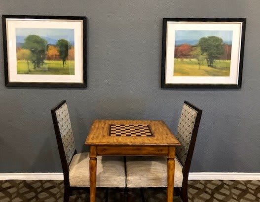 A small chess table with two chairs, framed by landscape paintings on the wall.