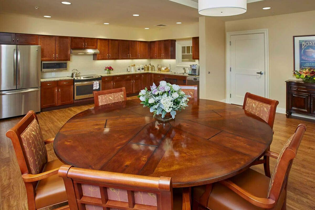 A spacious kitchen with wooden cabinetry and a round wooden dining table adorned with a flower arrangement.