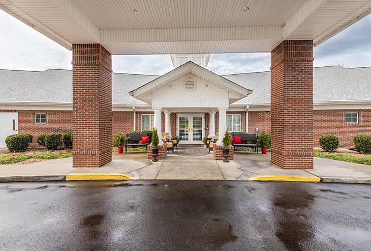 The front entrance of a brick building with outdoor seating and a covered driveway.