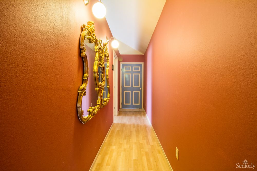 A vibrant hallway with red walls, a decorative mirror, and wooden flooring.
