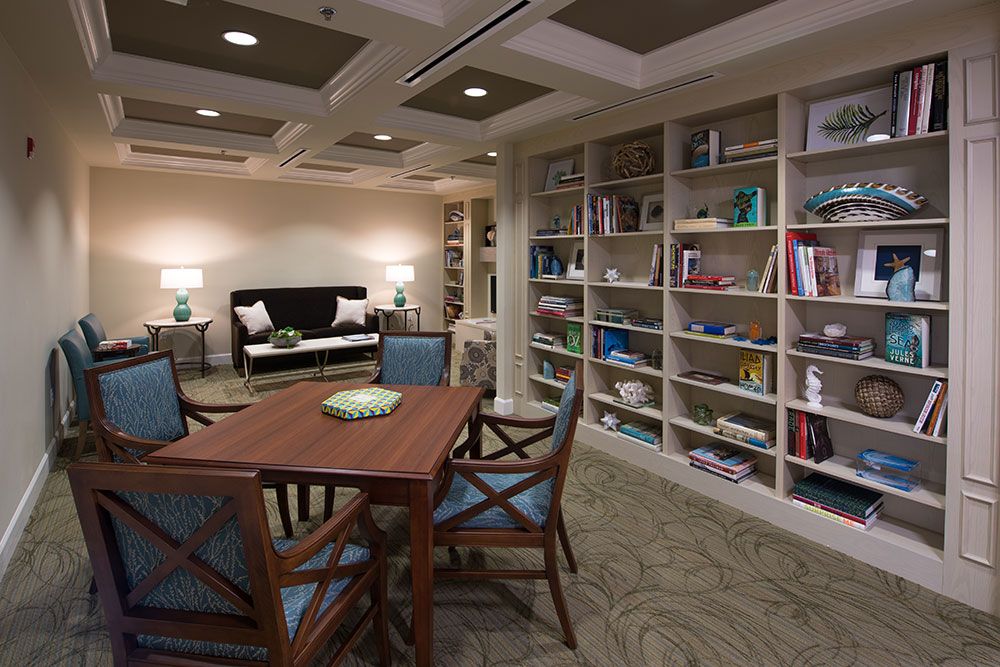 A cozy library interior featuring bookshelves, a seating area with a table and chairs, and soft lighting.