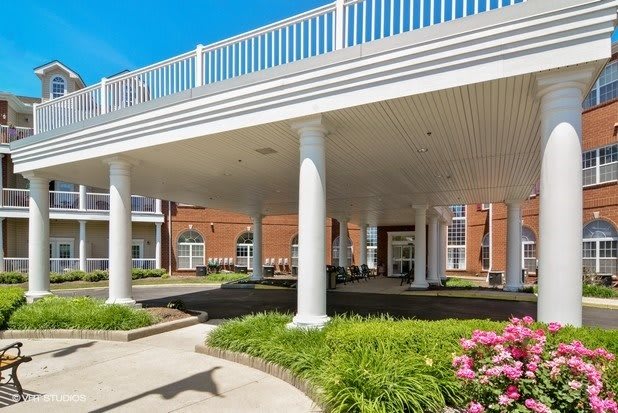 A building entrance with white columns and landscaped surroundings under a clear blue sky.