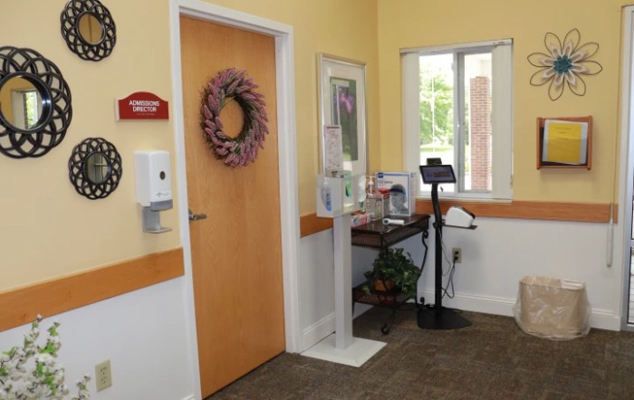 A welcoming entrance with a wreath-adorned door, hand sanitizer, and a small table by the window.