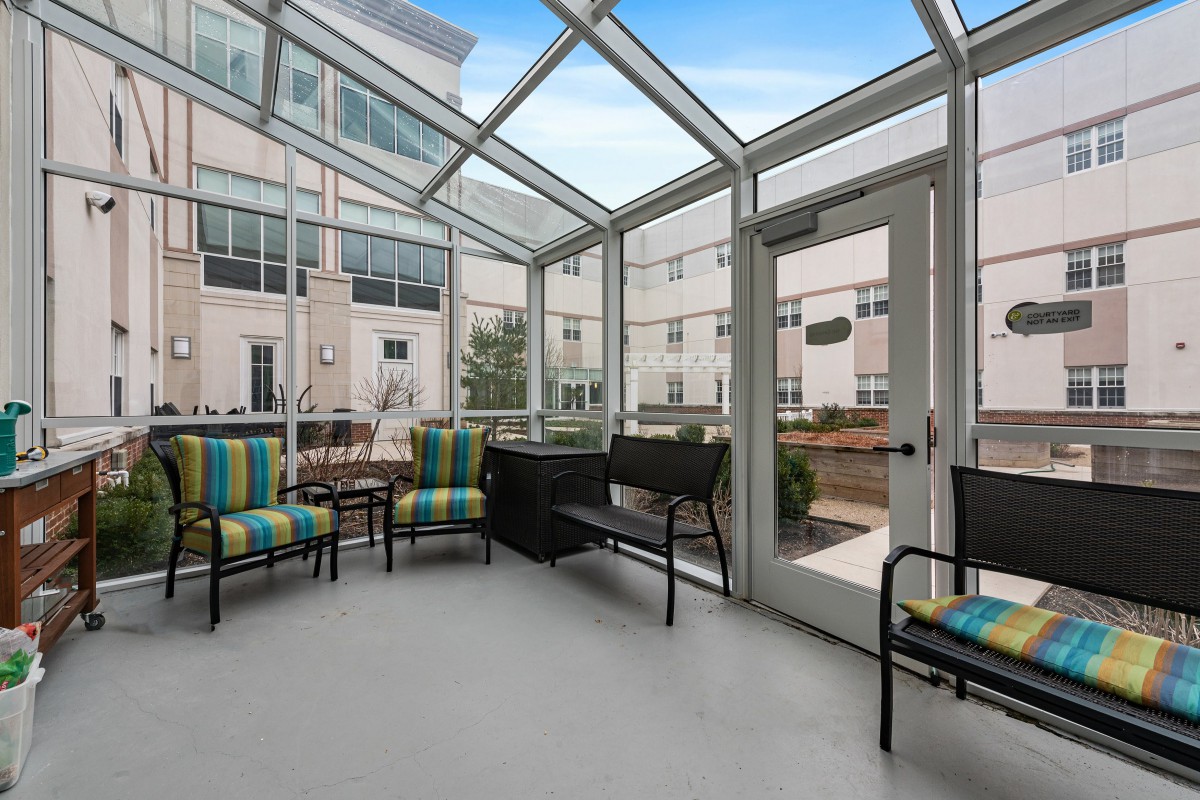 A glass-enclosed patio area with colorful chairs and tables in front of an apartment building.