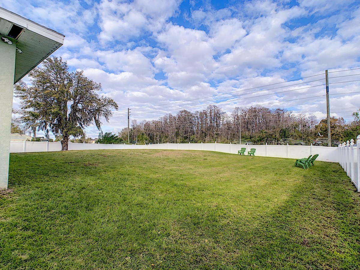 A spacious backyard with a green lawn and scattered trees under a cloudy sky.