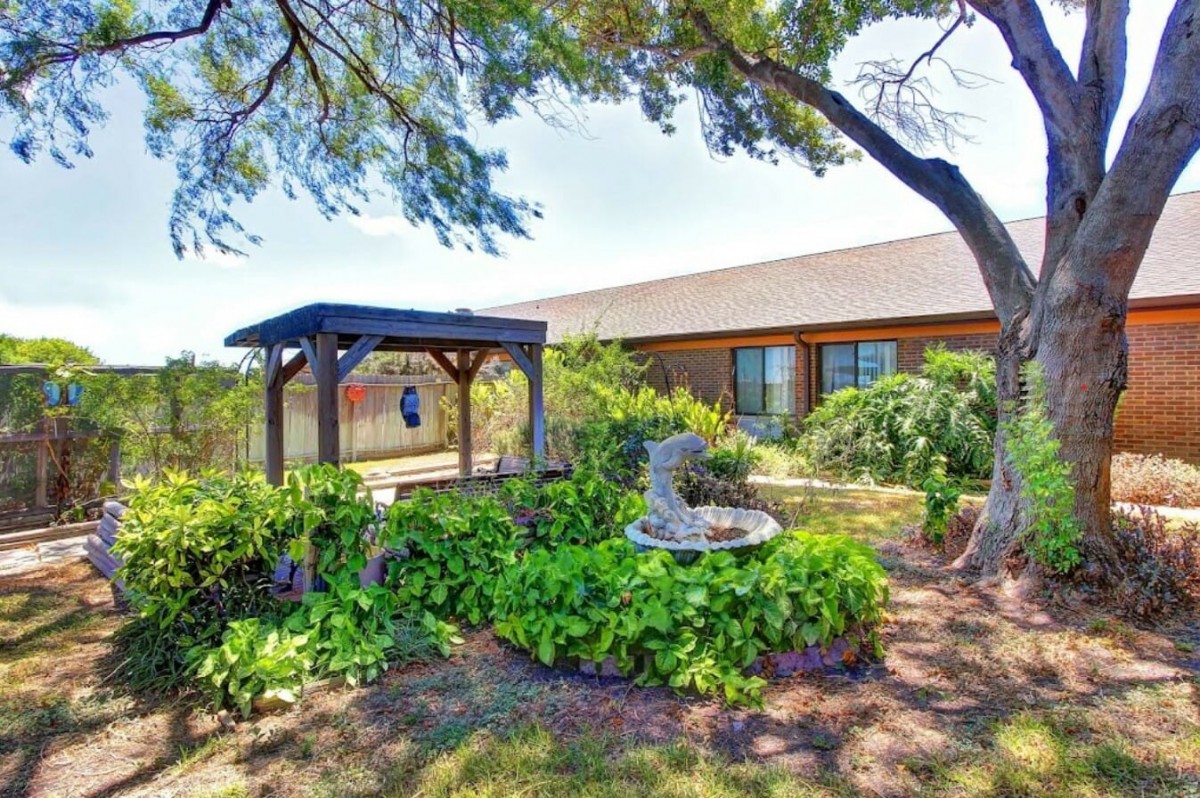 A scenic garden with a gazebo and fountain, surrounded by lush greenery next to a house.