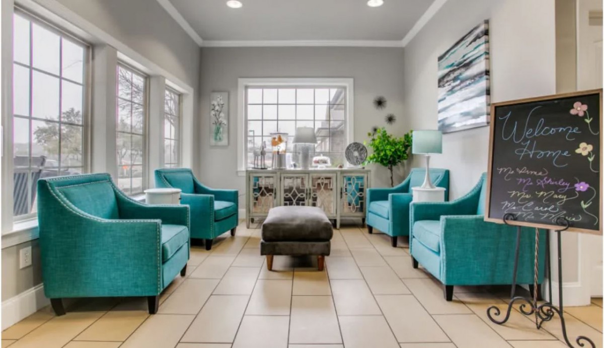 A modern living space with teal armchairs and a central ottoman, featuring large windows and stylish decor.
