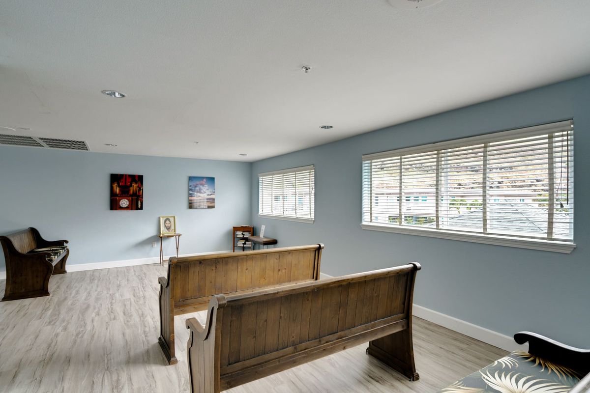 A simple room with light blue walls featuring a wooden bench, large windows, and two paintings on the wall.