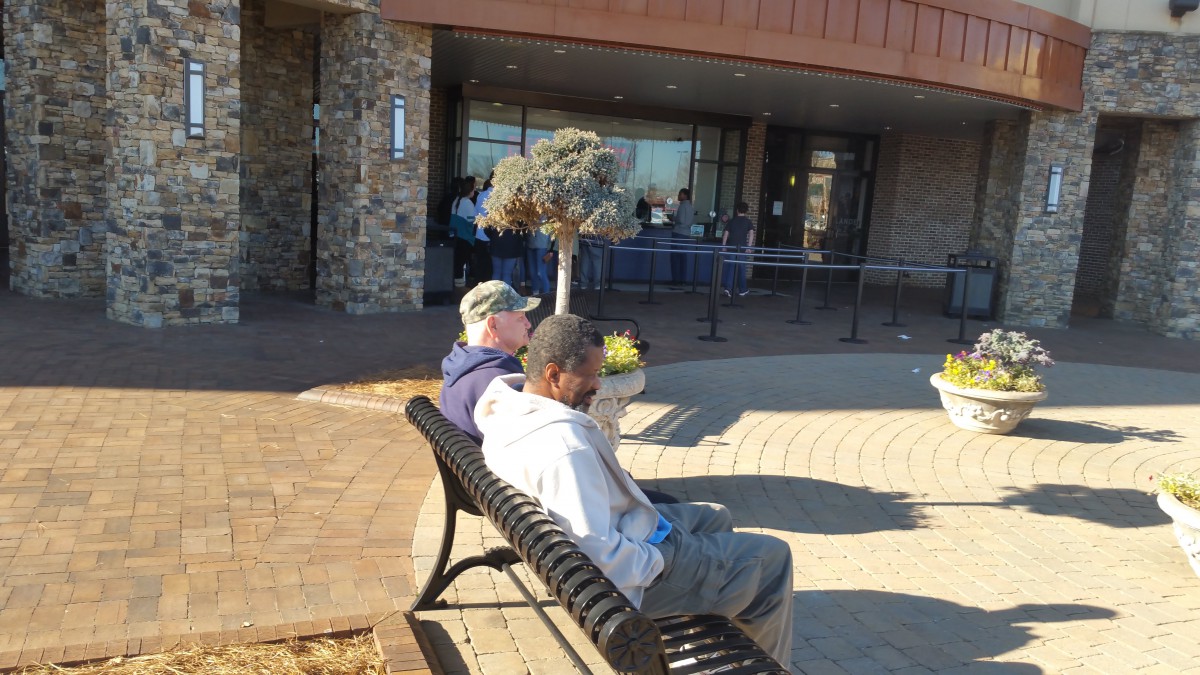 Two people sitting on a bench outside a building on a sunny day.