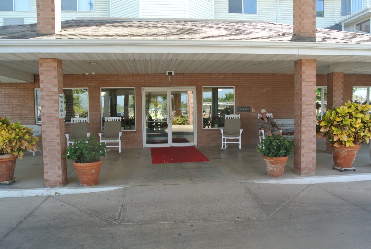 A building entrance featuring a red carpet, with chairs and potted plants on either side of the glass doors.