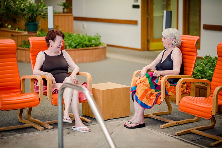 Two women sitting in chairs, engaging in conversation indoors.