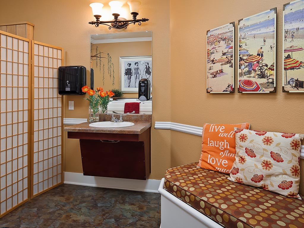 A well-decorated bathroom with a floating sink, wall mirror, and decorative cushions on a bench.